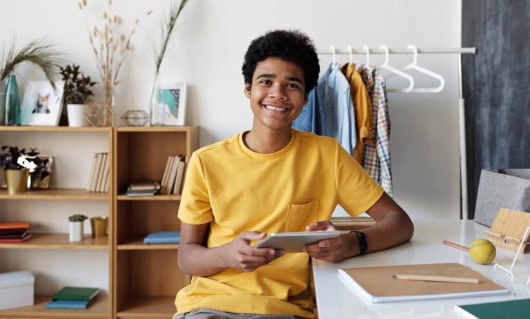 boy in a yellow shirt sitting in his room using a tablet