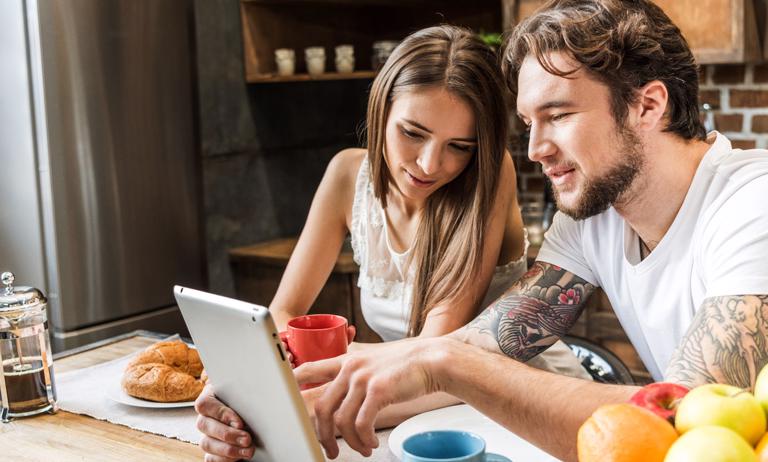 Photo of young couple looking at tablet and eating breakfast