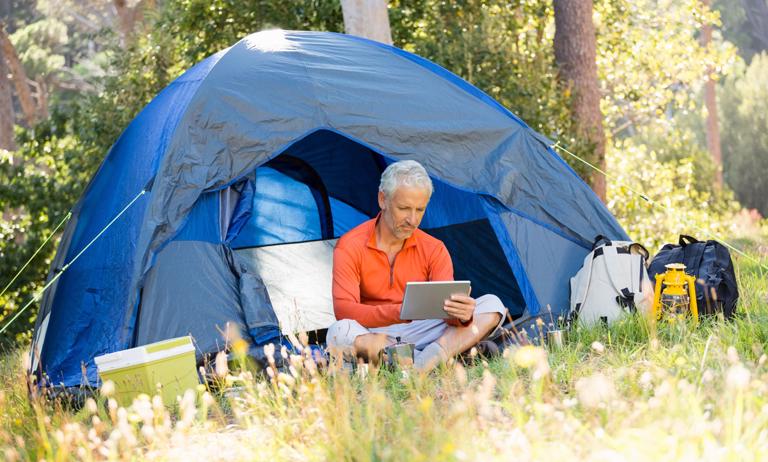 Photo of a man using tablet at a camp site